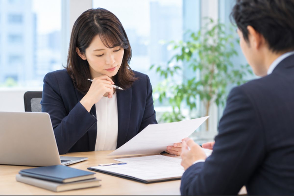 転職エージェントと求職者が机を挟んで書類を確認し、内定後の雇用条件や今後の入所について相談している様子